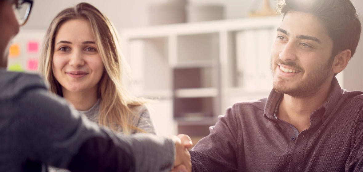 Young couple shake hands with a business person