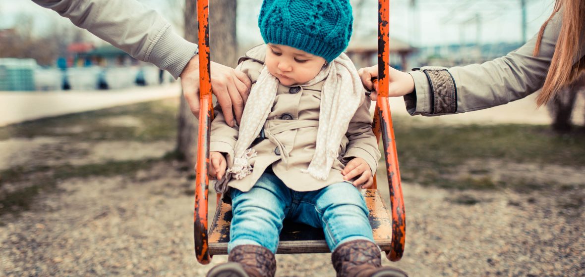 Child on a swing being pushed by two adults
