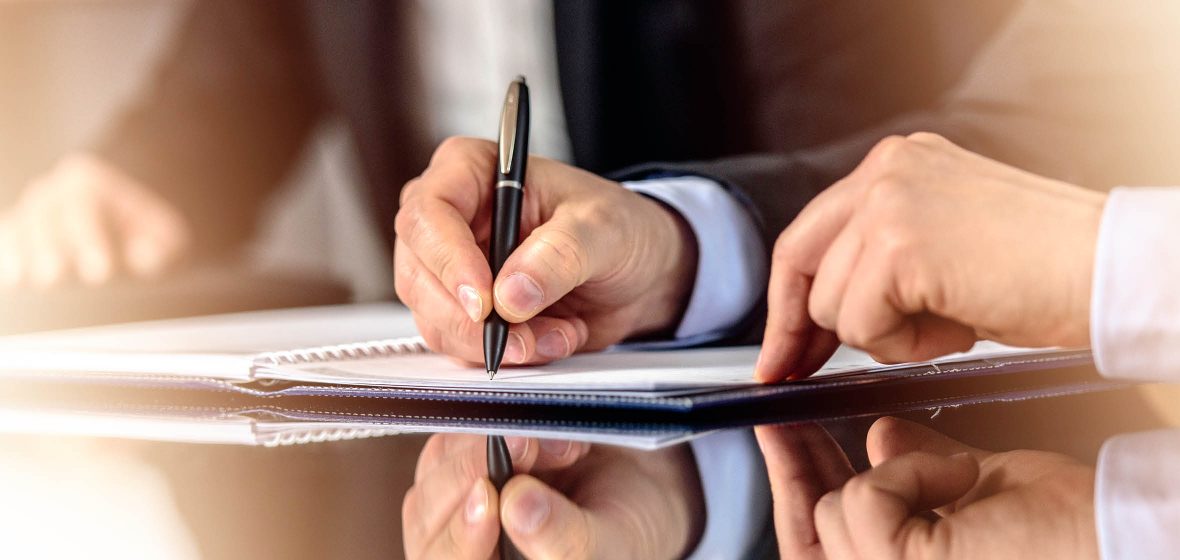 Man signs a document, witness by a second man