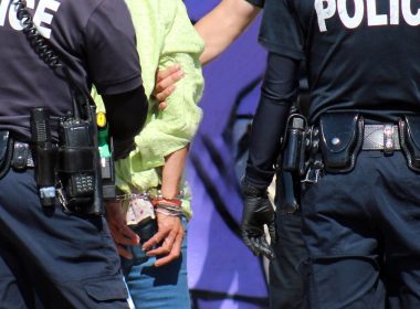 three police officers escorting a handcuffed male