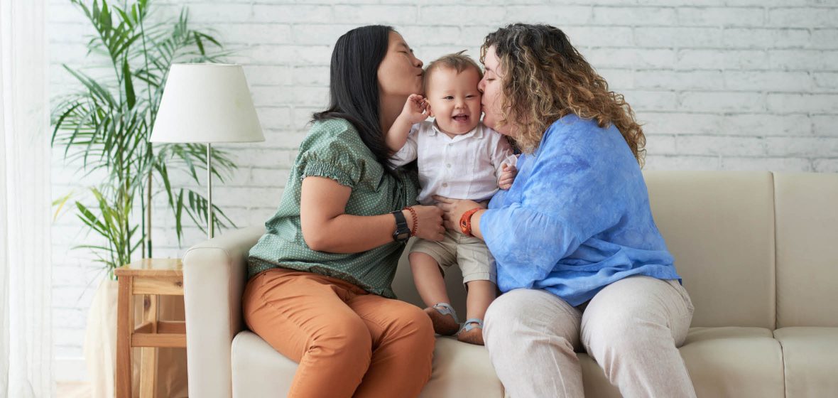 Two women sitting on the couch holding a child