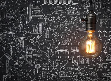 One light bulb shining on a chalkboard with sketches