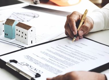 Man signs a contract on a desk, next to scale models of houses