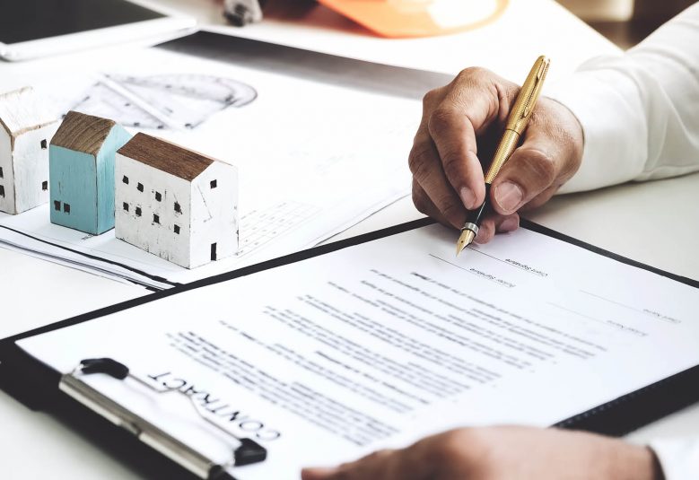 Man signs a contract on a desk, next to scale models of houses