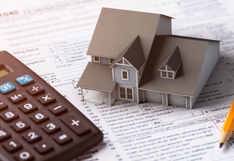 Scale model of a house sits on top of a a checklist on a desk, next to a pencil and a calculator.