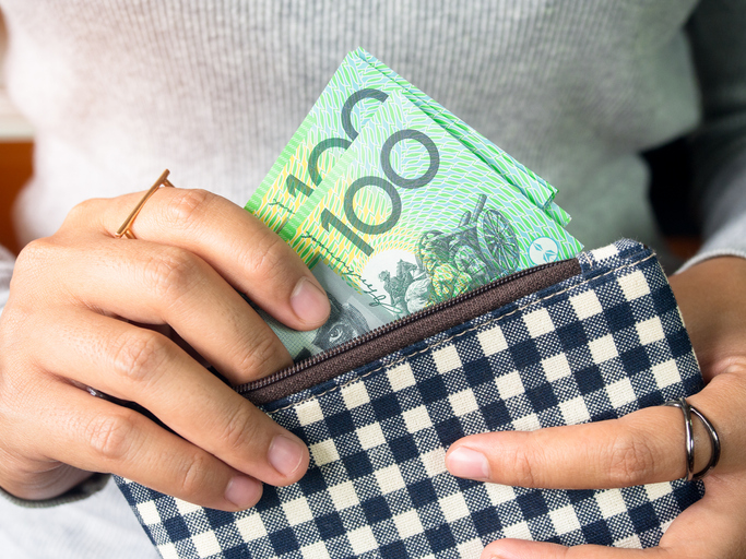 Woman putting Australian bank notes into wallet.