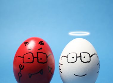 Close-up of two eggs, one white, one red, against blue background