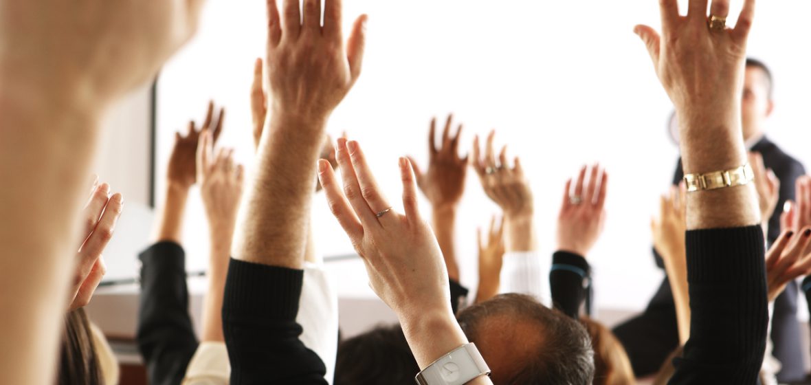 Big audience of people raising their hands to vote in favor of a topic.