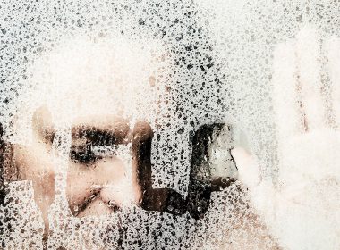 Woman with hand on glass, next to where she has written the word 'Help"