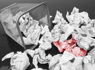 A lot of wrinkled paper laying in and around a wastepaper basket