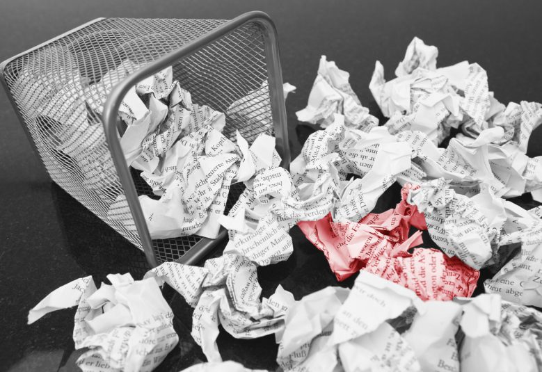 A lot of wrinkled paper laying in and around a wastepaper basket