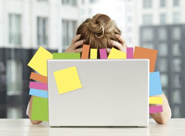 Exhausted businesswoman sits in front of a laptop covered in post-it notes