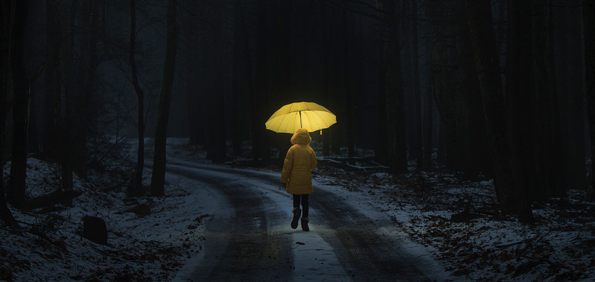 Child in a yellow raincoat, carrying a yellow umbrella walking on a road
