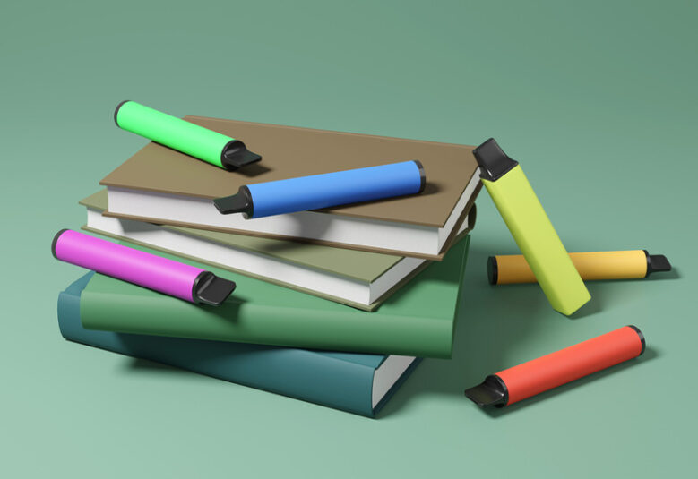 photo of books with colourful vapes lying on them resembling pens